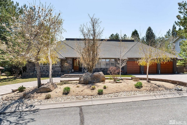 single story home featuring driveway, stone siding, and a garage