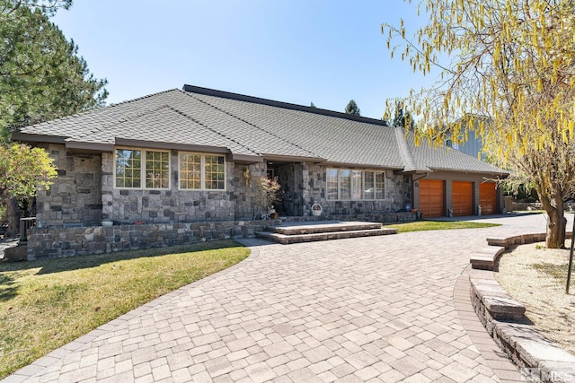 view of front facade featuring stone siding, an attached garage, a front yard, and decorative driveway