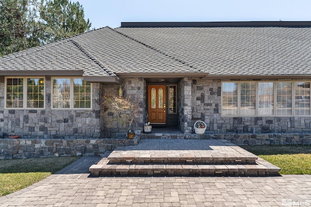 view of exterior entry featuring stone siding and a shingled roof