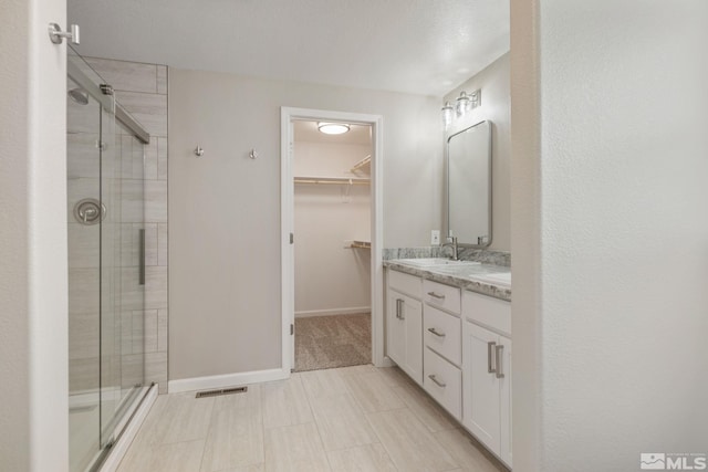 full bathroom with a shower stall, a walk in closet, vanity, baseboards, and visible vents