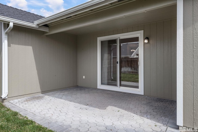 property entrance with a patio area and a shingled roof