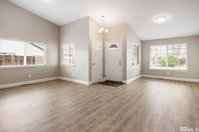 entrance foyer featuring baseboards, lofted ceiling, a chandelier, and light wood-style floors
