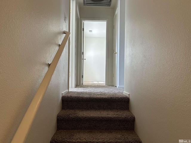 staircase with a textured wall and carpet floors