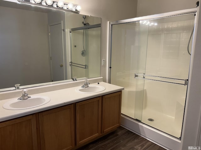 bathroom with double vanity, a shower stall, wood finished floors, and a sink