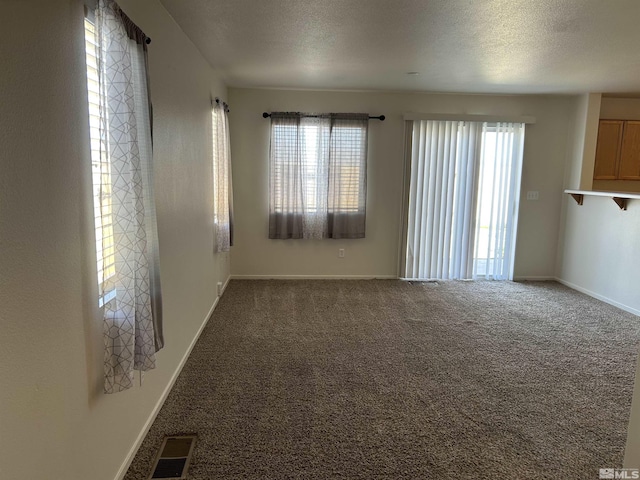 carpeted empty room featuring a textured ceiling, visible vents, and baseboards