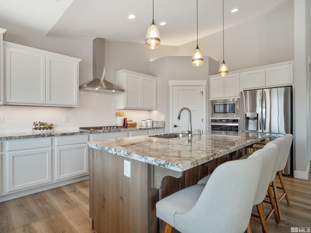 kitchen with a sink, white cabinetry, backsplash, wall chimney range hood, and appliances with stainless steel finishes