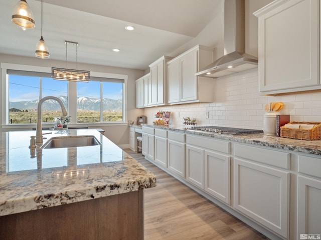 kitchen featuring stainless steel gas stovetop, wall chimney range hood, a sink, light wood-style flooring, and white cabinetry