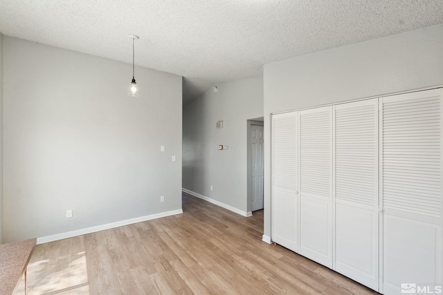 unfurnished bedroom featuring a textured ceiling, a closet, light wood finished floors, and baseboards