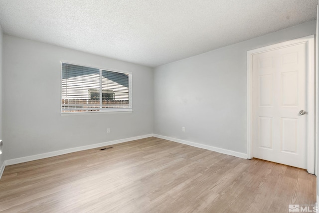 empty room featuring a textured ceiling, light wood-style flooring, visible vents, and baseboards
