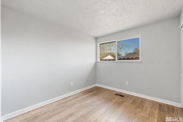 empty room with a textured ceiling, light wood-style flooring, visible vents, and baseboards