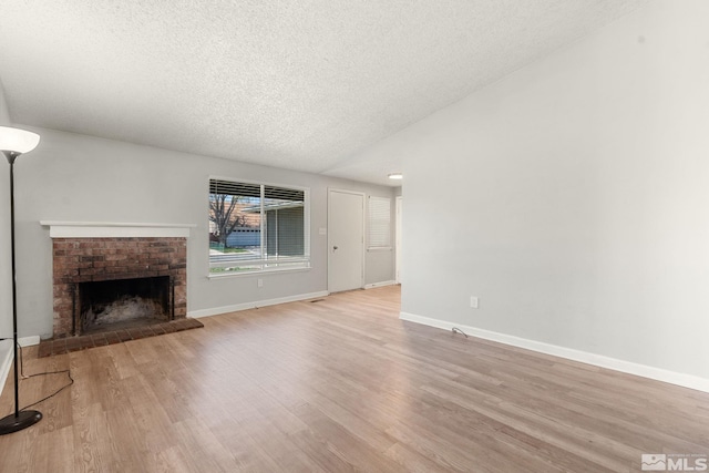 unfurnished living room with vaulted ceiling, a textured ceiling, light wood-type flooring, a fireplace, and baseboards