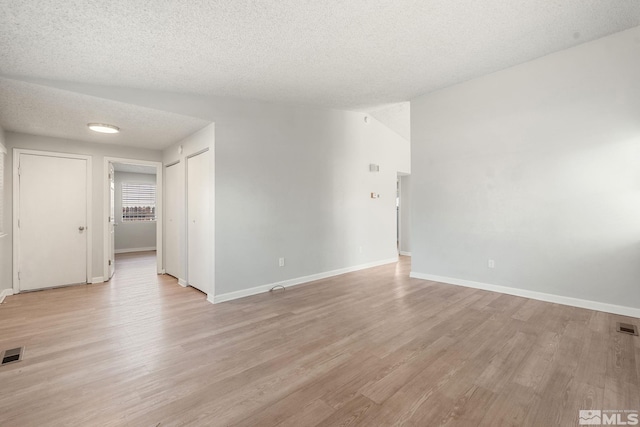 unfurnished room with baseboards, light wood-style floors, visible vents, and a textured ceiling