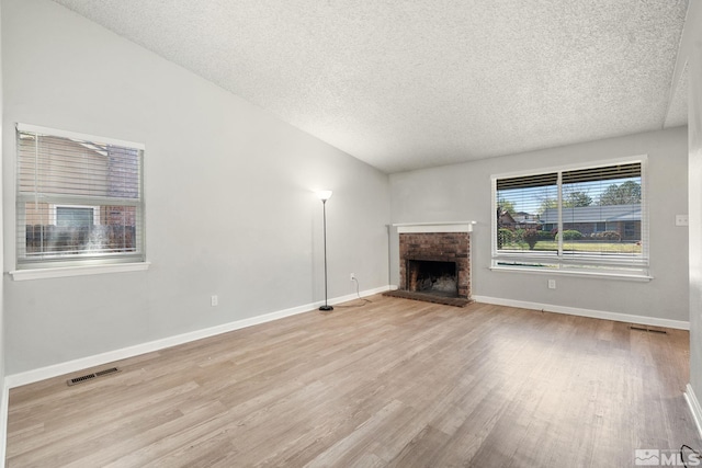 unfurnished living room with a brick fireplace, wood finished floors, visible vents, baseboards, and a textured ceiling