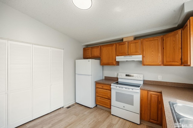 kitchen featuring lofted ceiling, under cabinet range hood, a sink, white appliances, and brown cabinetry