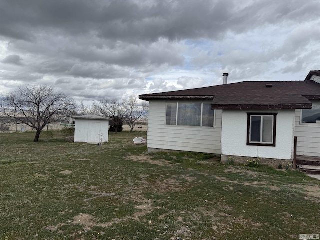 rear view of house featuring a lawn, an outbuilding, roof with shingles, and a shed