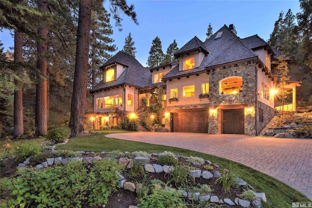 view of front of property featuring stone siding, an attached garage, curved driveway, stucco siding, and a front lawn