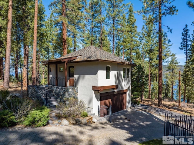 view of side of property featuring stairway, a garage, decorative driveway, roof with shingles, and stucco siding
