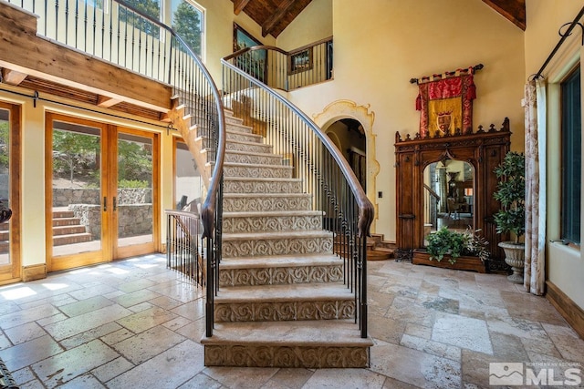 stairway with high vaulted ceiling, french doors, stone tile flooring, and plenty of natural light