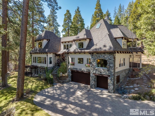 french provincial home with stairway, a garage, a balcony, driveway, and stone siding