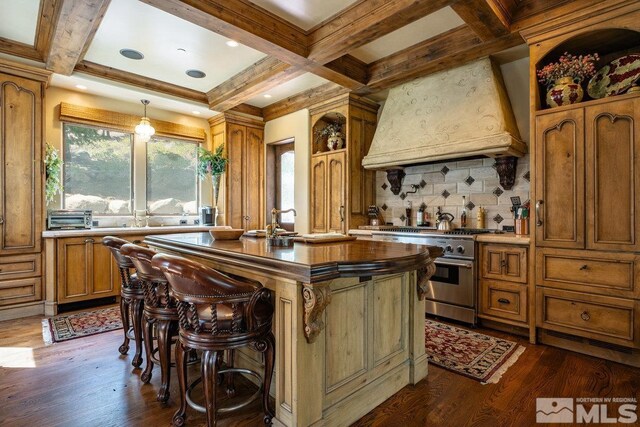 kitchen featuring coffered ceiling, premium range hood, stainless steel range, and brown cabinetry