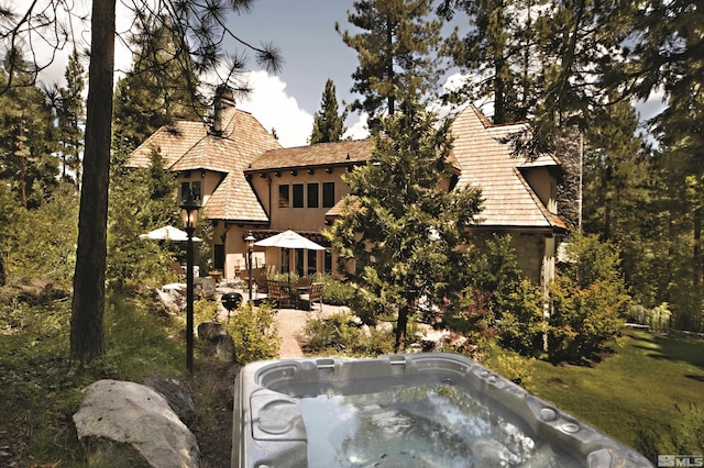 view of front of house with a chimney, stucco siding, a hot tub, and a patio area