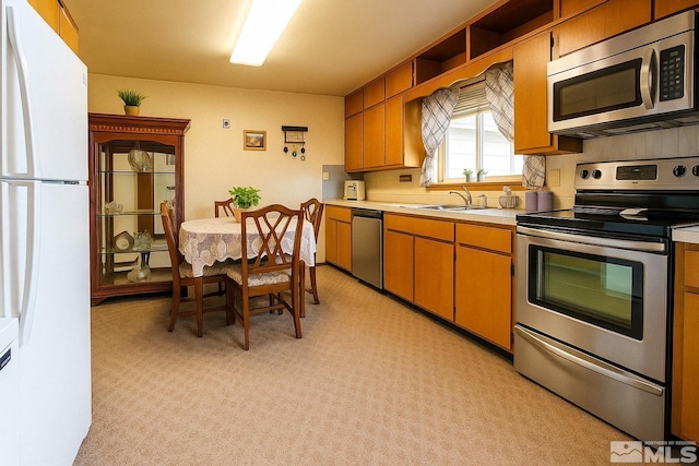 kitchen featuring a sink, brown cabinets, stainless steel appliances, light countertops, and light colored carpet