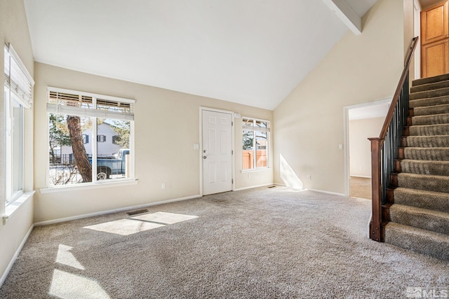 unfurnished living room with plenty of natural light, high vaulted ceiling, carpet, and stairway