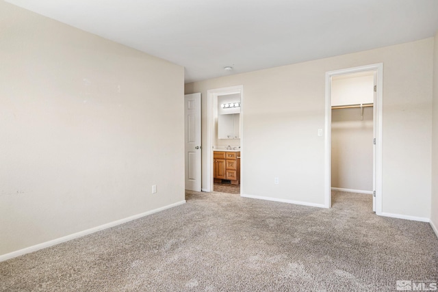unfurnished bedroom featuring a spacious closet, light carpet, ensuite bathroom, and baseboards