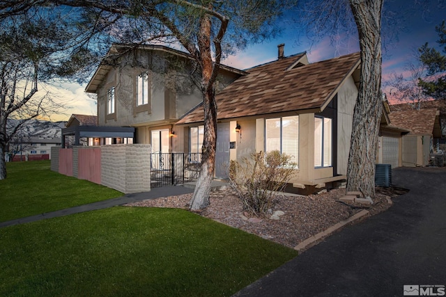 view of front of house with stucco siding, fence, cooling unit, and a lawn