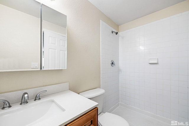 full bath featuring tiled shower, vanity, and toilet
