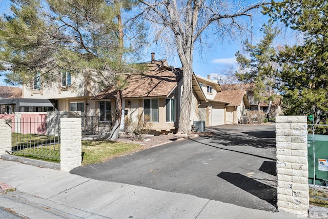 view of property featuring central AC unit, aphalt driveway, fence, a garage, and stucco siding