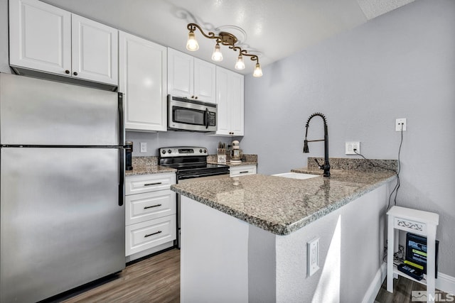 kitchen featuring stainless steel appliances, a peninsula, a sink, dark wood-style flooring, and white cabinetry