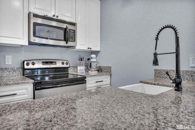 kitchen featuring white cabinets, light stone countertops, stainless steel appliances, and a sink