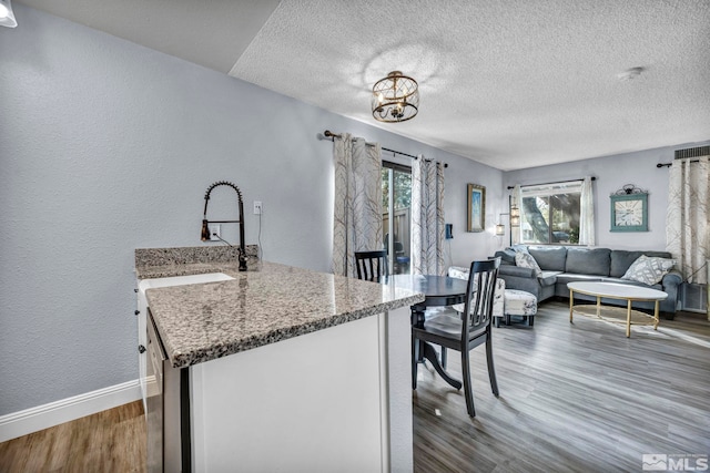 kitchen featuring wood finished floors, a sink, stone counters, a textured ceiling, and open floor plan