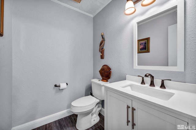 bathroom featuring wood finished floors, vanity, a textured wall, baseboards, and toilet