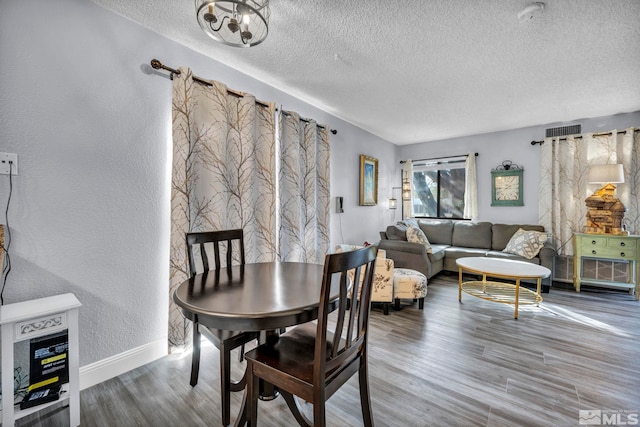 dining area with wood finished floors, a textured ceiling, a textured wall, baseboards, and visible vents