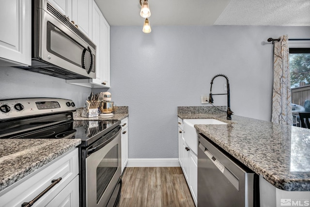 kitchen with light wood finished floors, baseboards, white cabinets, a peninsula, and appliances with stainless steel finishes