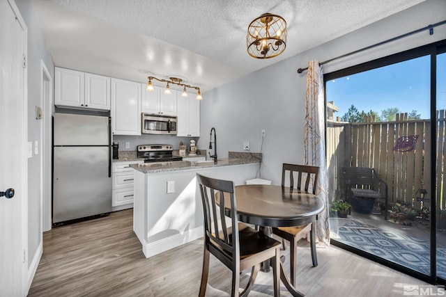 kitchen featuring stainless steel appliances, wood finished floors, a sink, a peninsula, and white cabinetry
