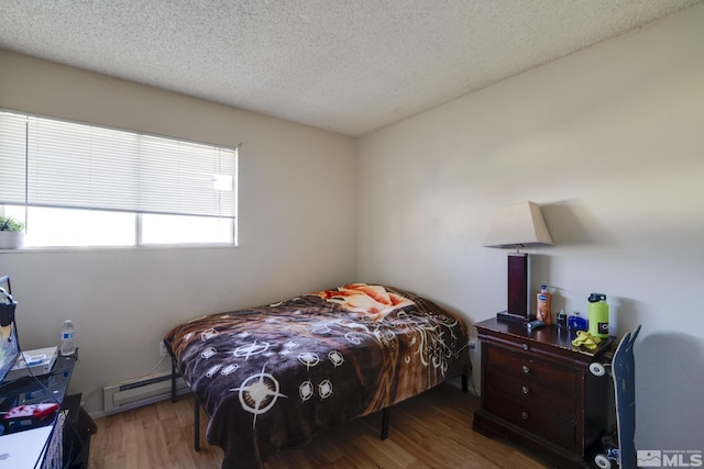 bedroom featuring baseboard heating, wood finished floors, and a textured ceiling