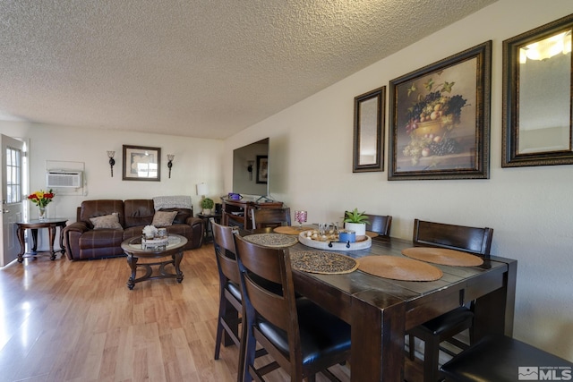 dining area with a textured ceiling, a wall mounted AC, and light wood-style flooring