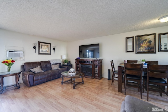 living room featuring light wood-style flooring, a wall unit AC, a textured ceiling, and a fireplace