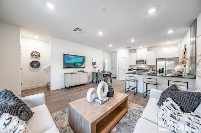 living room with baseboards, light wood-style flooring, visible vents, and recessed lighting