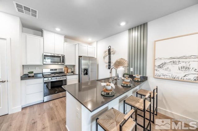 kitchen featuring light wood finished floors, dark countertops, visible vents, a sink, and appliances with stainless steel finishes