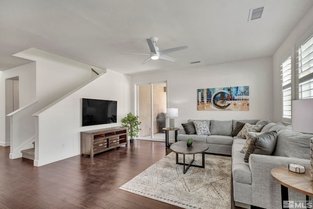 living room featuring dark wood finished floors, visible vents, stairs, and ceiling fan