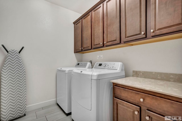 washroom featuring washing machine and clothes dryer, cabinet space, and baseboards