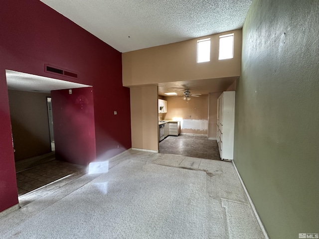 interior space with a textured ceiling, visible vents, baseboards, a towering ceiling, and ceiling fan