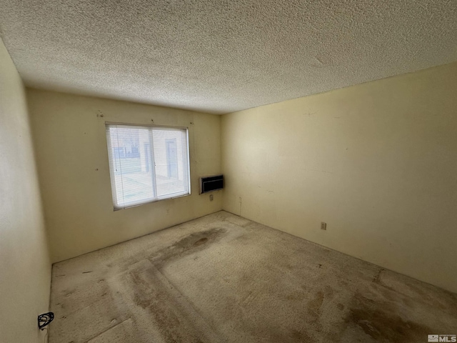 spare room featuring heating unit, a textured ceiling, and carpet