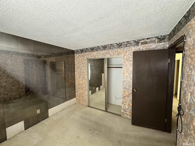 unfurnished bedroom featuring carpet floors, a textured ceiling, visible vents, and a closet