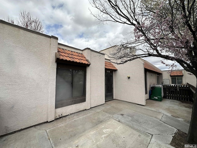 back of house with stucco siding, a tile roof, fence, and a patio