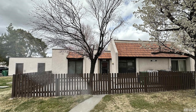 view of front facade with a fenced front yard, a tiled roof, and stucco siding